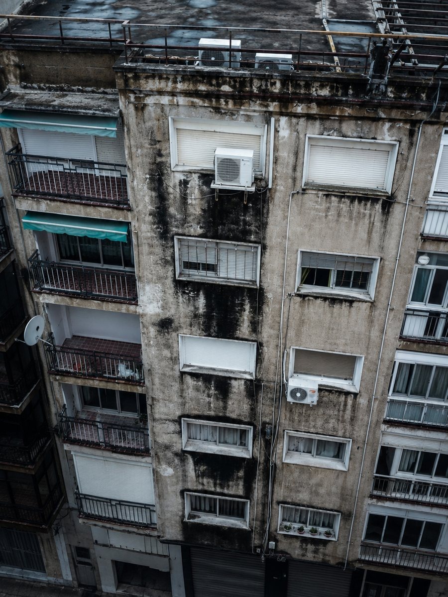 Fachada: documentación del daño visible Inspección visual de una fachada de viviendas con manchas oscuras y revestimiento deteriorado junto a ventanas y coronación